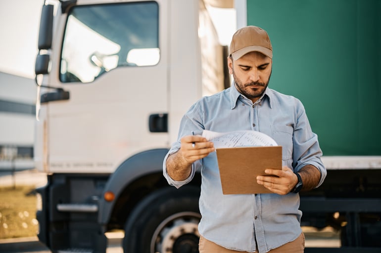 Man reading freight shipping manifest in front of a carrier truck